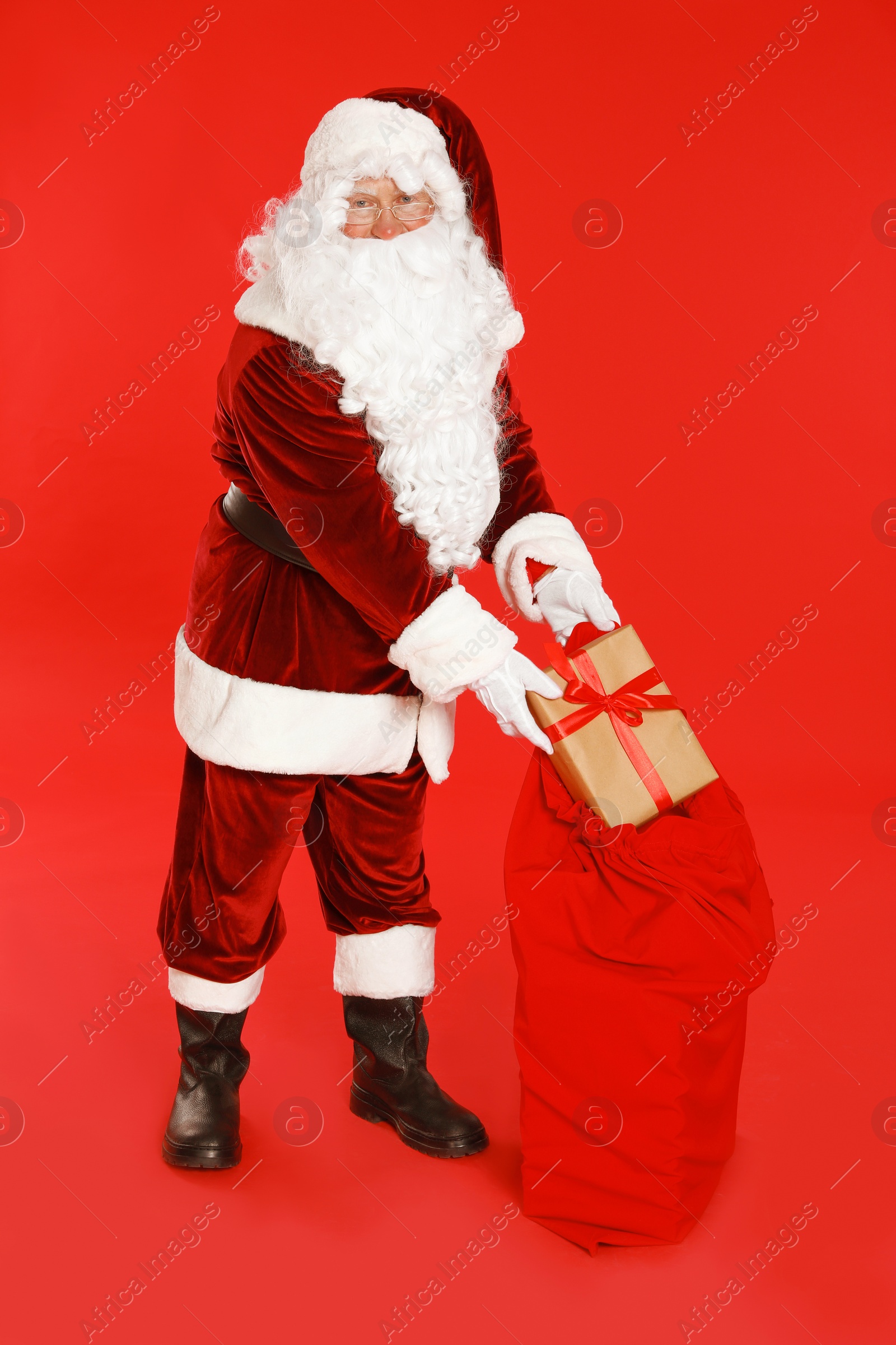 Photo of Authentic Santa Claus with sack and gift on red background