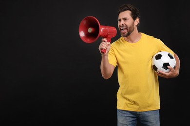 Photo of Emotional sports fan with soccer ball and megaphone on black background, space for text