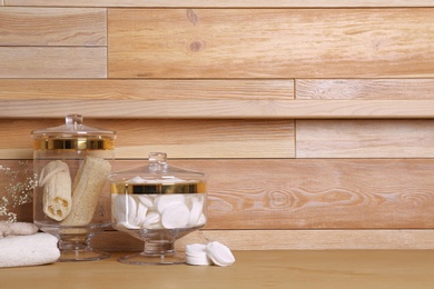 Photo of Composition of glass jar with cotton pads on table near wooden wall. Space for text