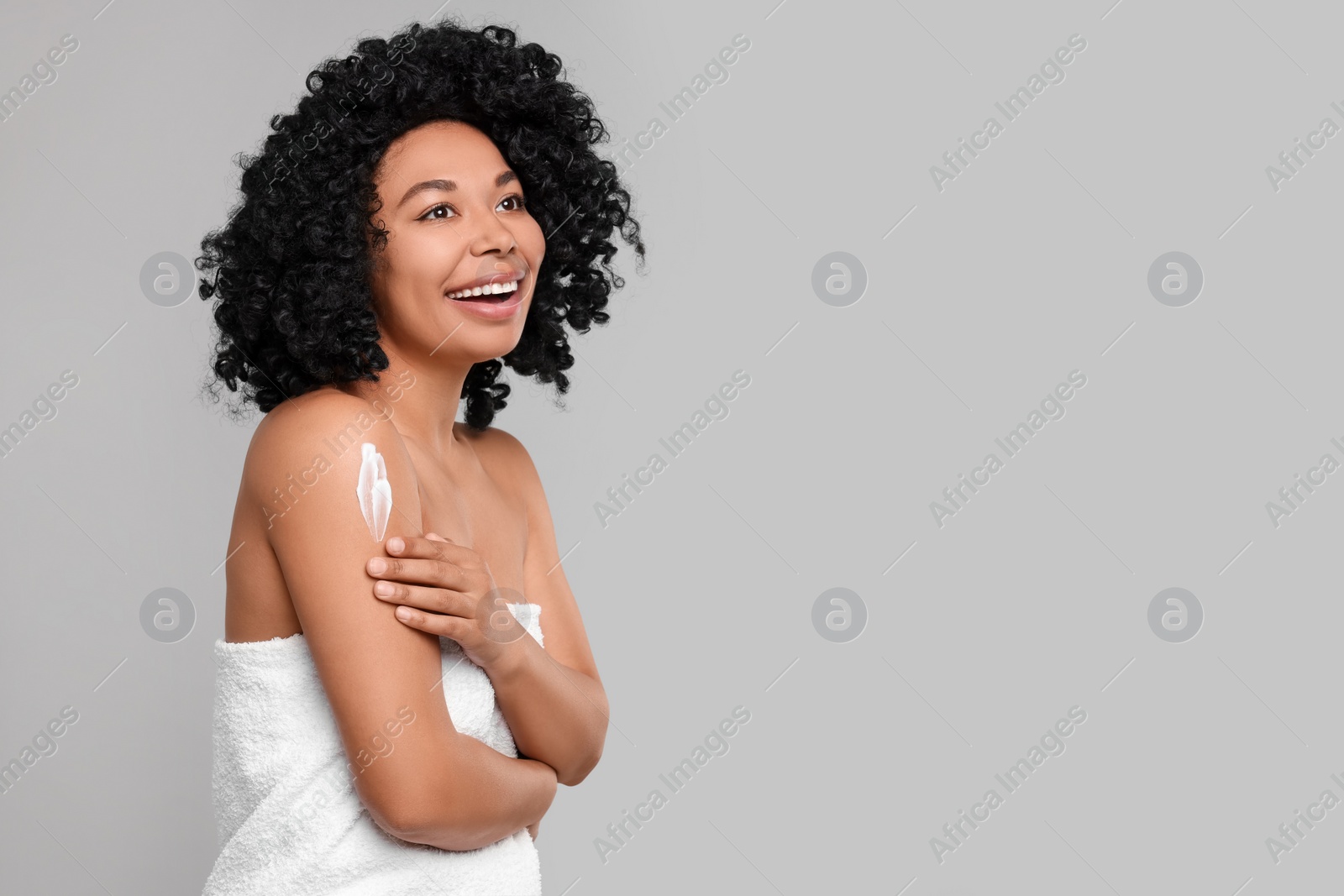 Photo of Young woman applying body cream onto shoulder on grey background. Space for text