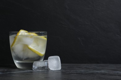 Photo of Glass of vodka with lemon slices and ice on grey table. Space for text
