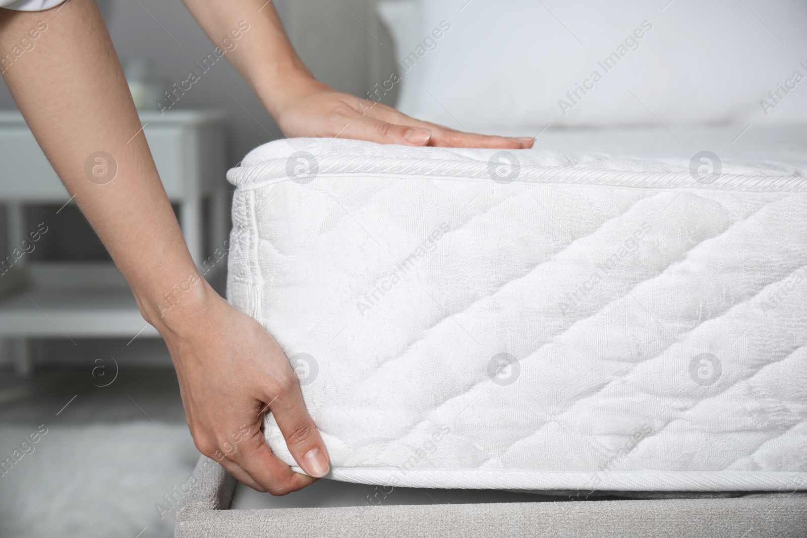 Photo of Woman putting soft white mattress on bed indoors, closeup