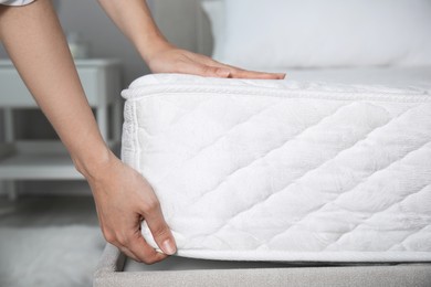 Woman putting soft white mattress on bed indoors, closeup