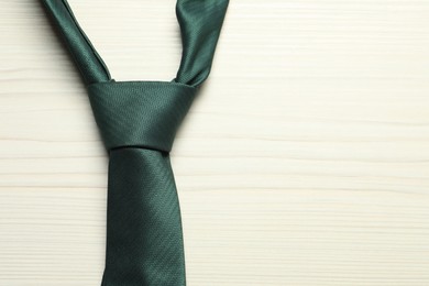 Photo of One green necktie on white wooden table, top view. Space for text