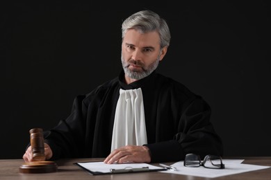 Judge with gavel and papers sitting at wooden table against black background