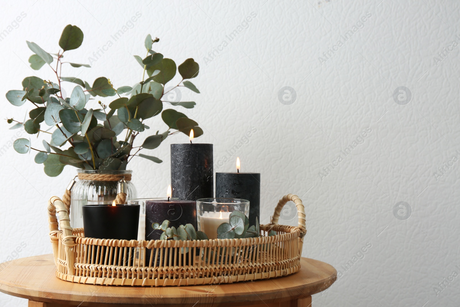 Photo of Tray with burning candles and green branches on table at white wall, space for text