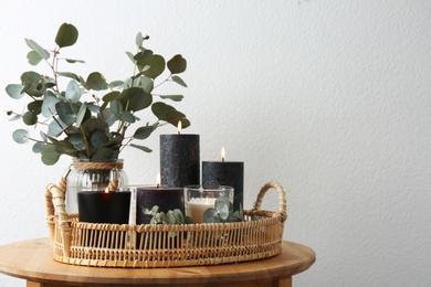 Tray with burning candles and green branches on table at white wall, space for text