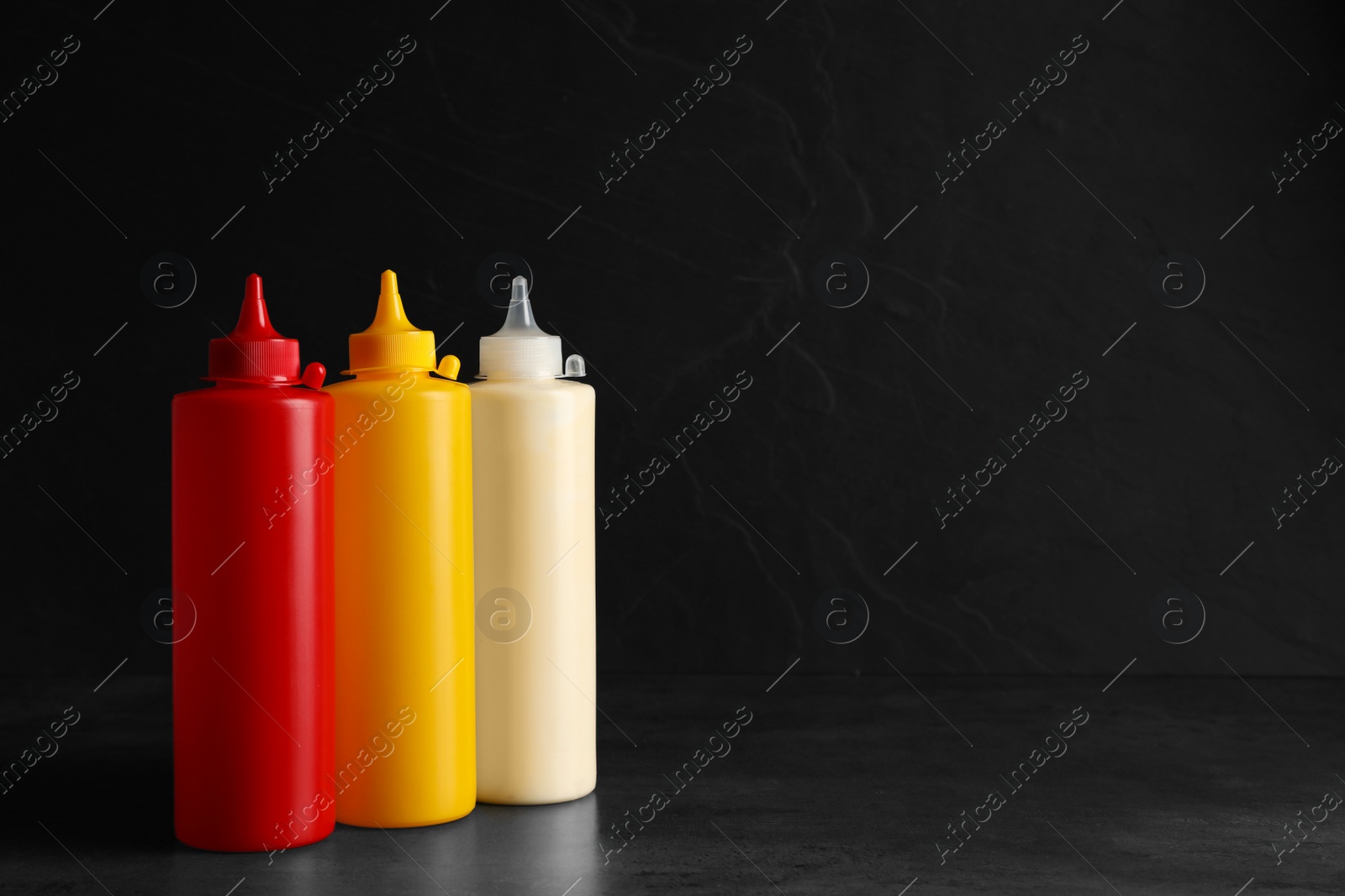 Photo of Ketchup, mustard and mayonnaise in squeeze bottles on grey table, space for text