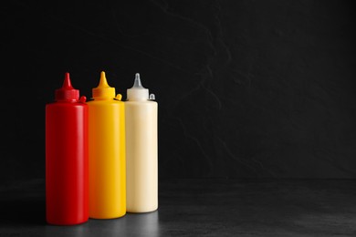Photo of Ketchup, mustard and mayonnaise in squeeze bottles on grey table, space for text
