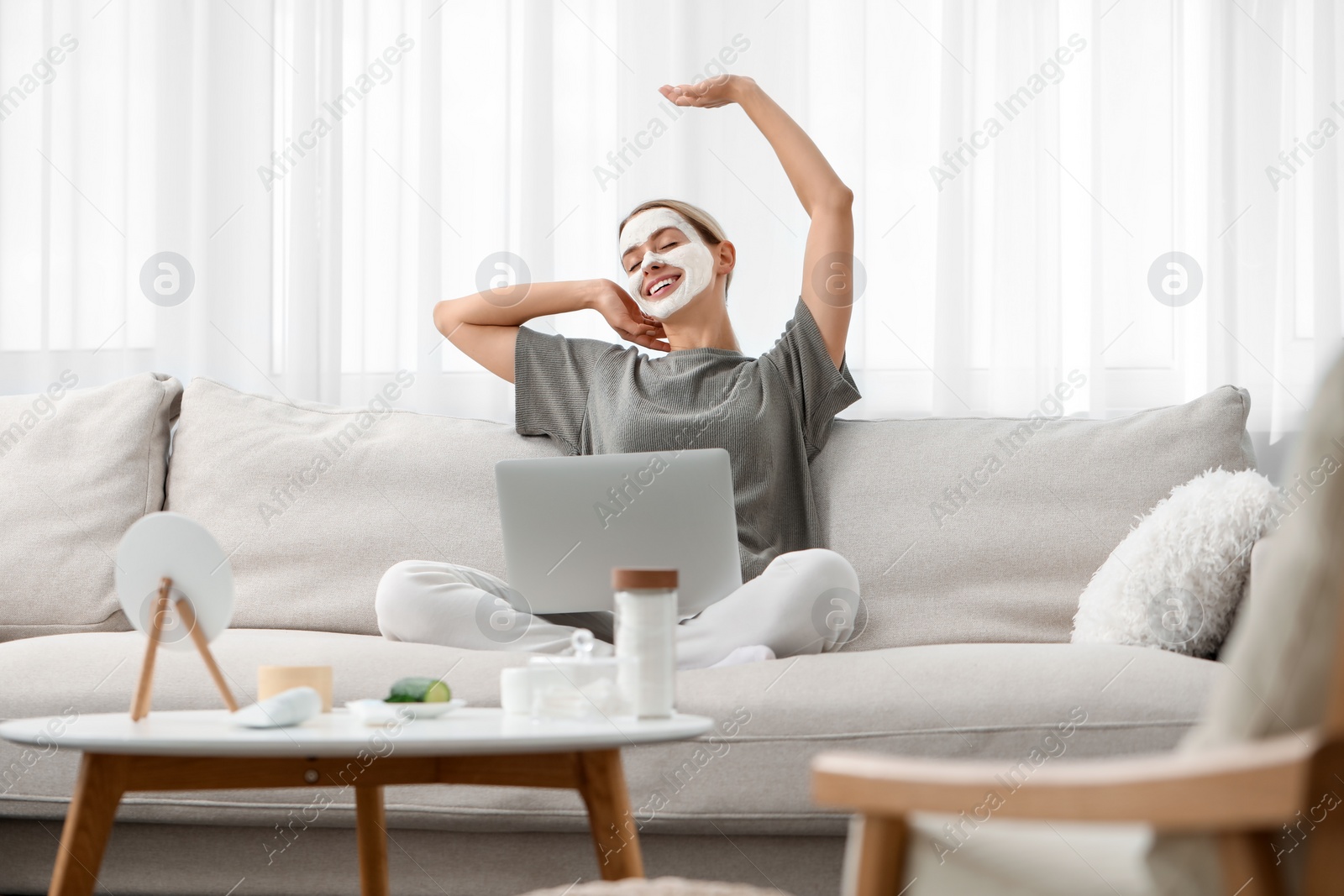 Photo of Young woman with face mask using laptop on sofa at home. Spa treatments