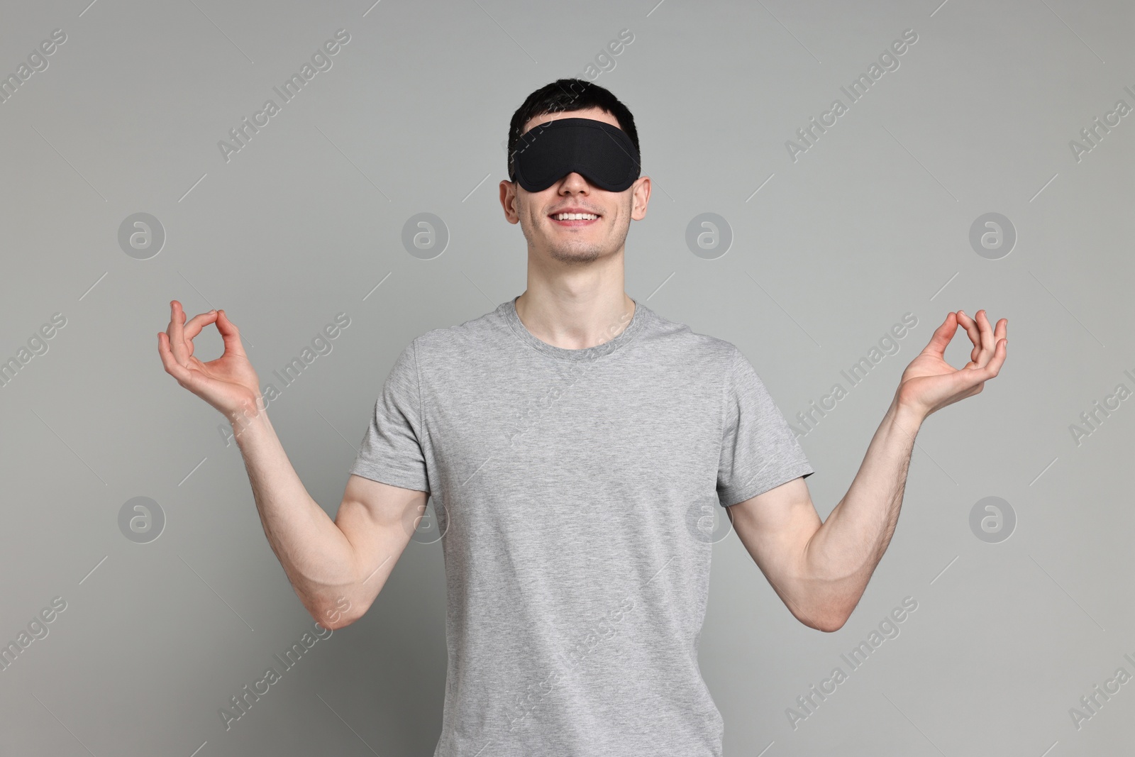 Photo of Man in pyjama and sleep mask meditating on grey background