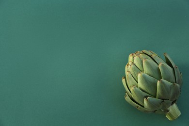 Whole fresh raw artichoke on green background, top view. Space for text