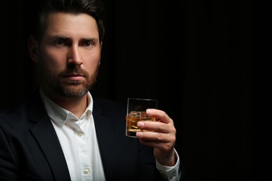 Photo of Man in suit holding glass of whiskey with ice cubes on black background. Space for text
