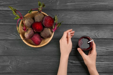 Photo of Woman with glass of delicious beet juice at grey wooden table, top view