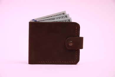 Stylish brown leather wallet with dollar banknotes on pink background