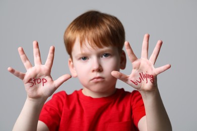 Photo of Boy showing hands with phrase Stop Bullying on light grey background, selective focus