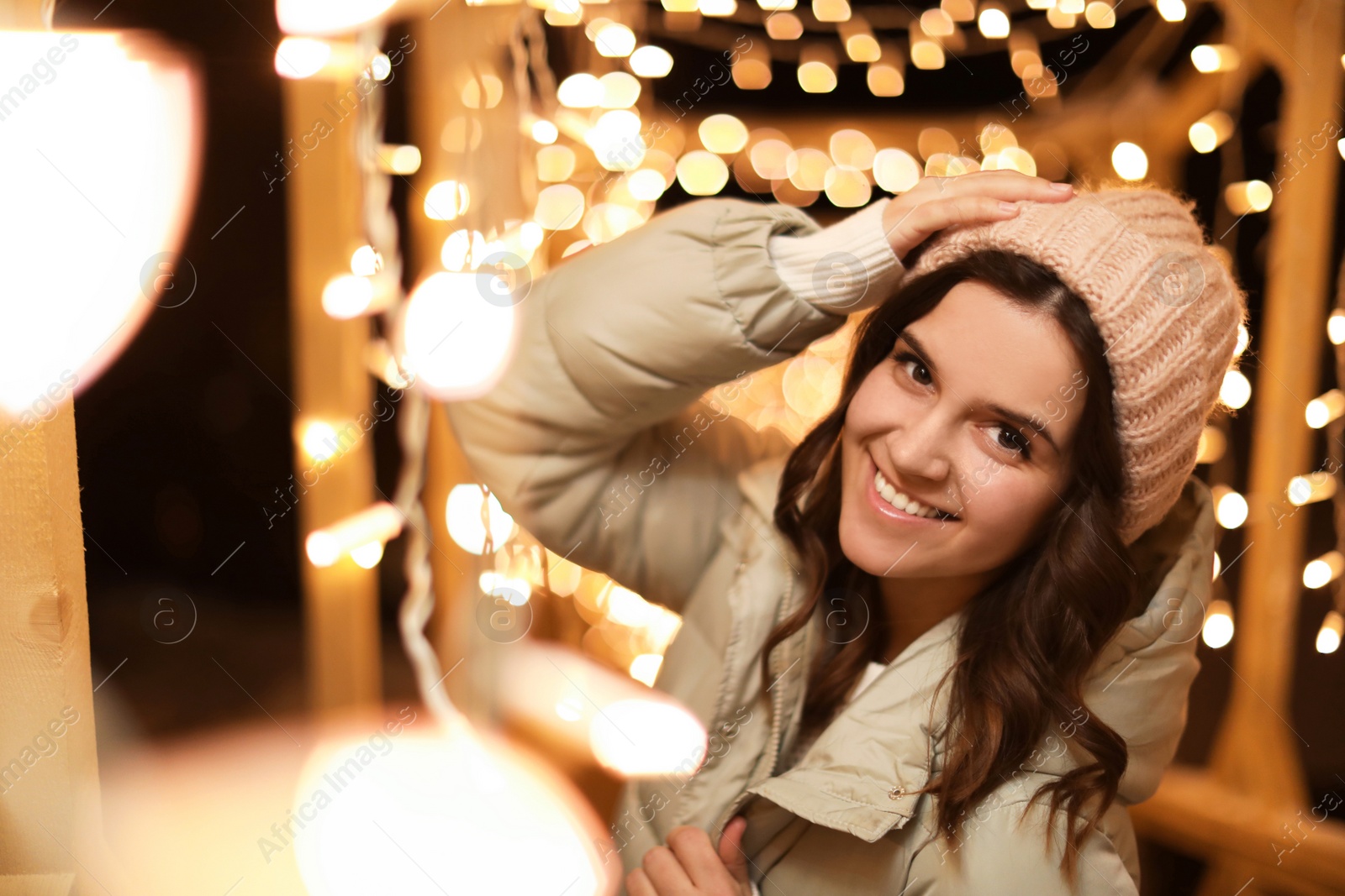 Photo of Beautiful young woman near festive lights outdoors. Winter vacation