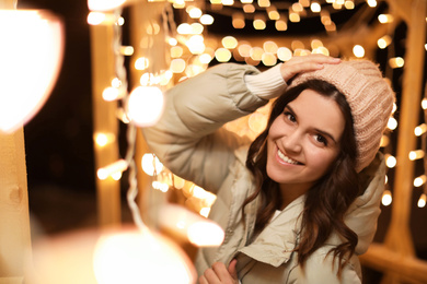 Photo of Beautiful young woman near festive lights outdoors. Winter vacation