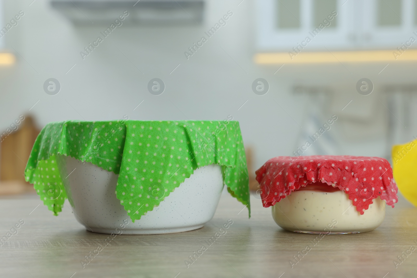 Photo of Bowls covered with beeswax food wraps on wooden table in kitchen