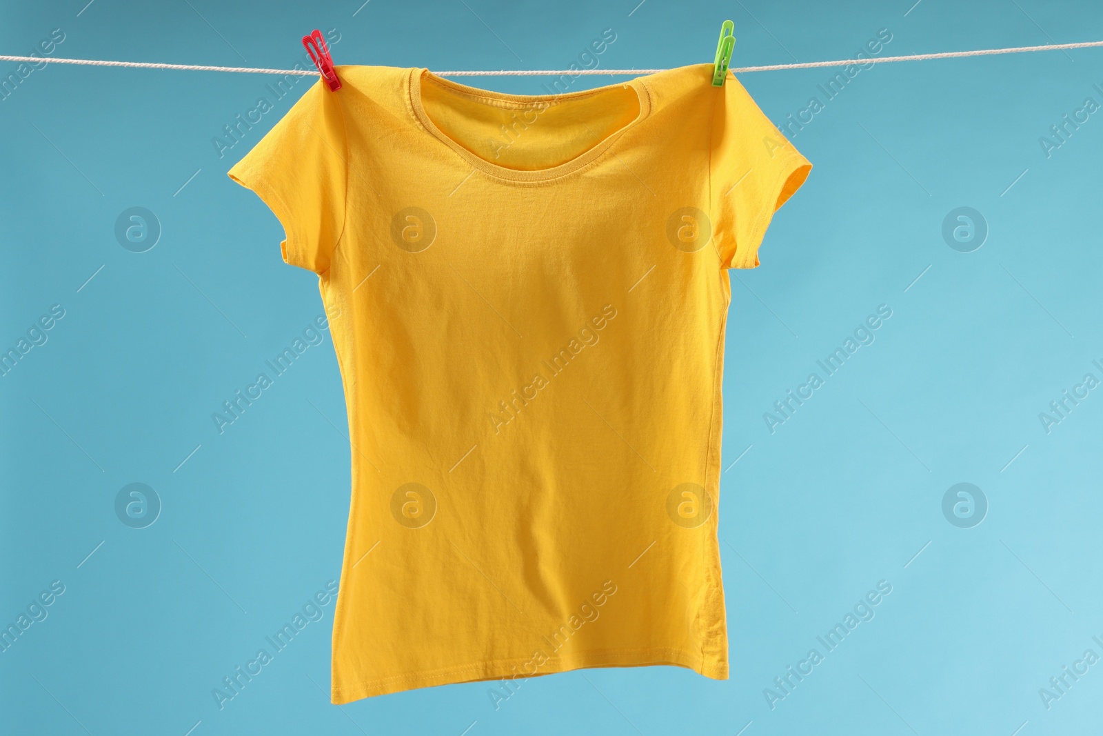 Photo of One yellow t-shirt drying on washing line against light blue background