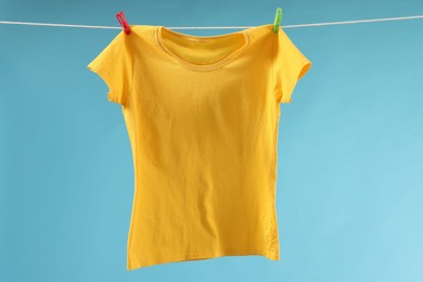 One yellow t-shirt drying on washing line against light blue background