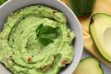 Bowl of delicious guacamole with parsley and fresh avocado on table, flat lay