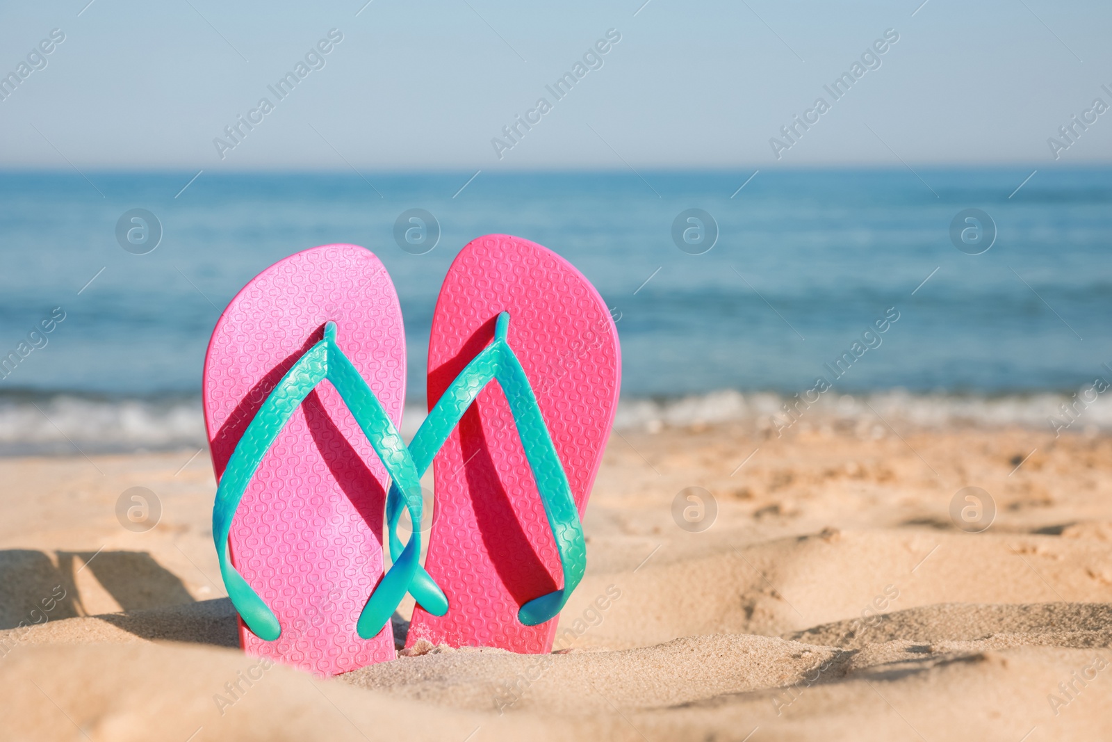 Photo of Stylish flip flops in sand on beach. Space for text