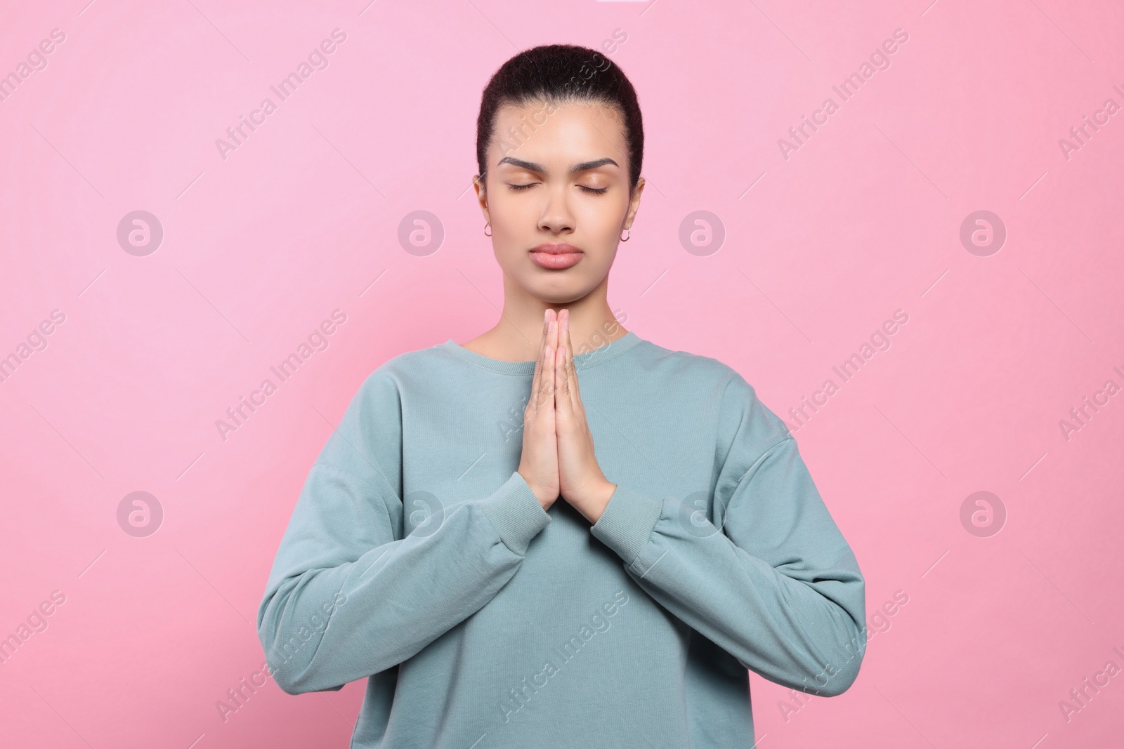 Photo of African American woman with clasped hands praying to God on pink background