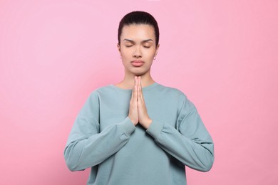 African American woman with clasped hands praying to God on pink background