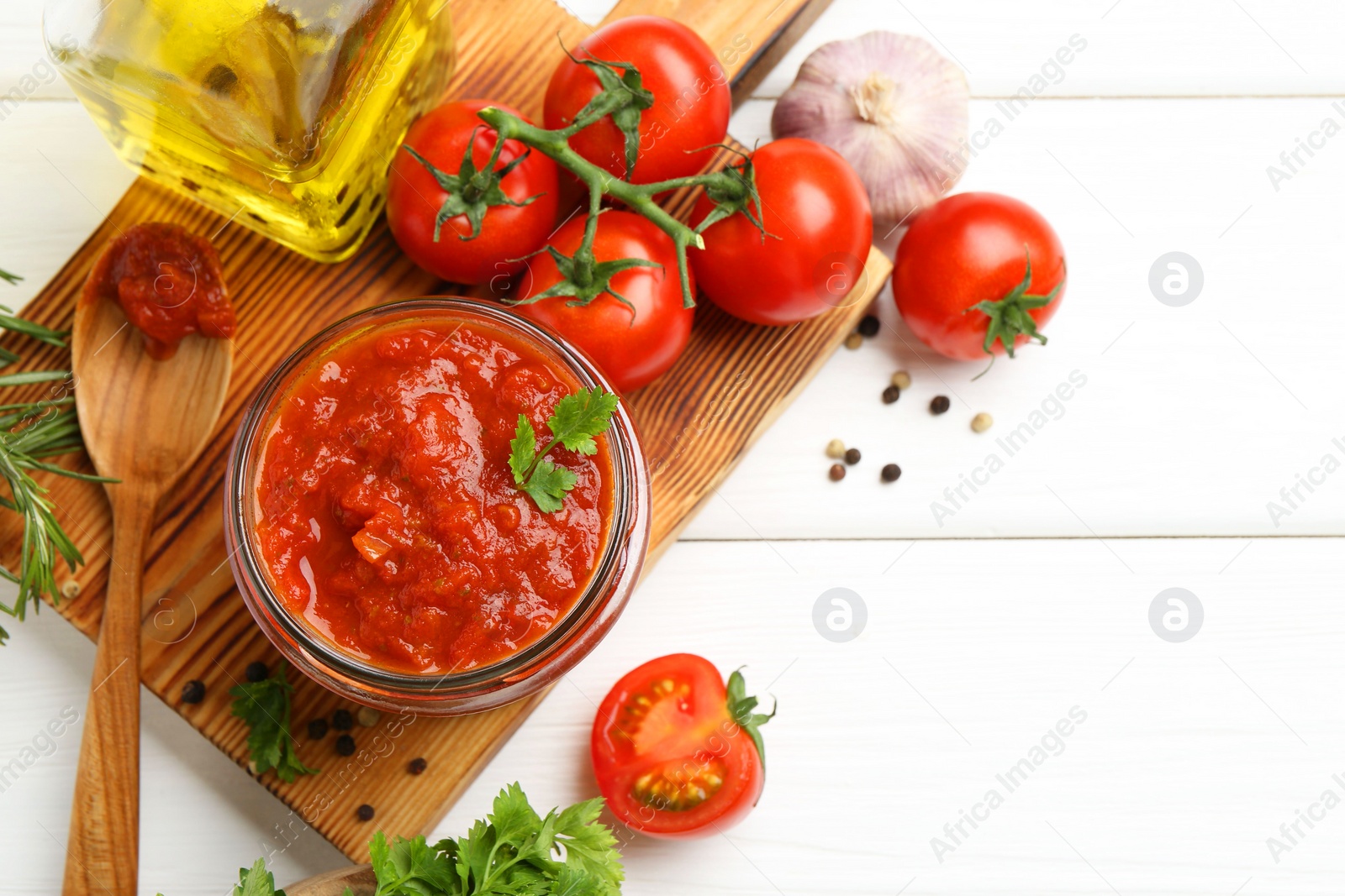 Photo of Homemade tomato sauce in jar, spoon and fresh ingredients on white wooden table, flat lay. Space for text