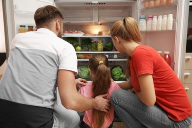 Young family choosing food in refrigerator at home