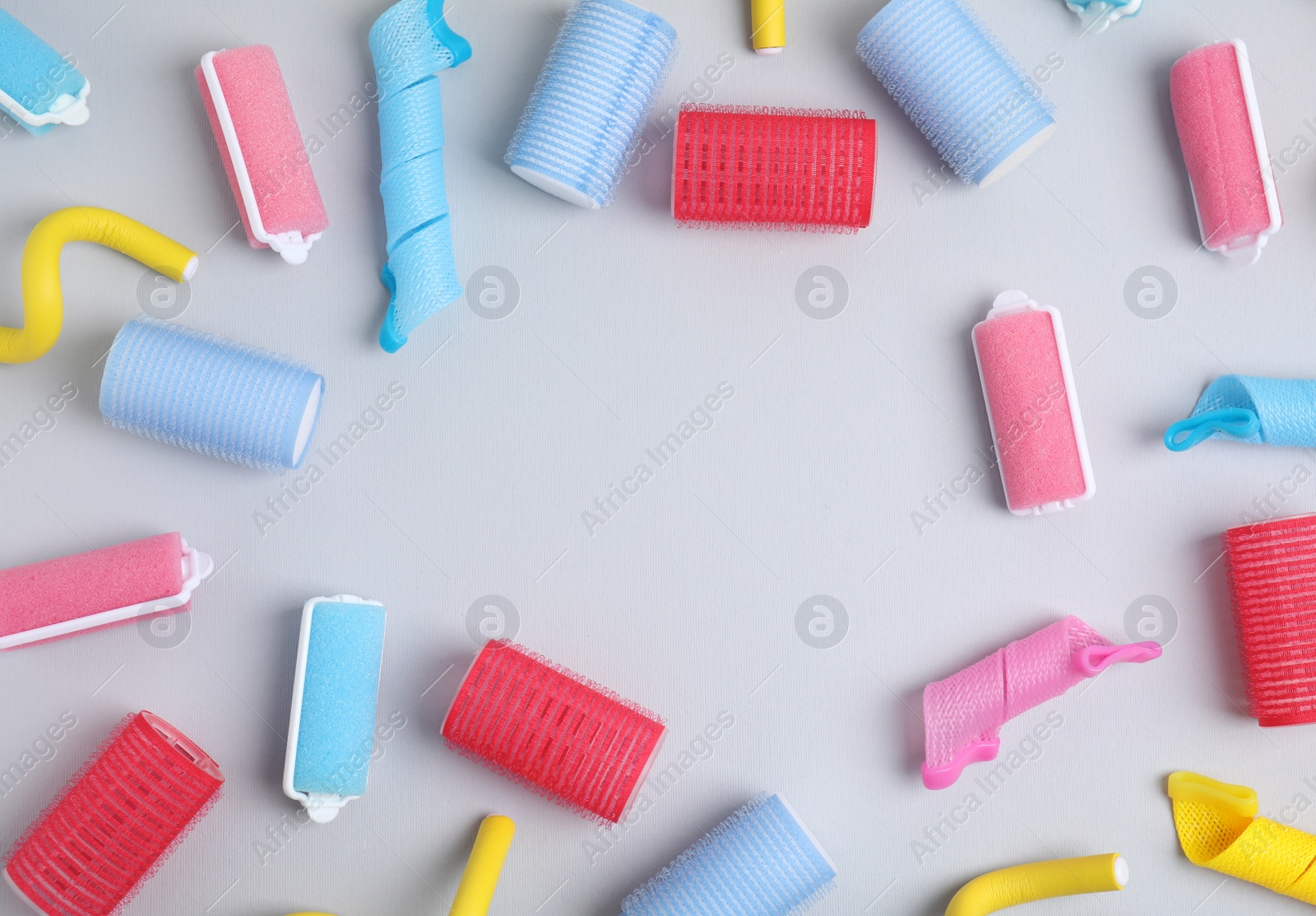 Photo of Frame of different hair curlers on light grey background, flat lay. Space for text