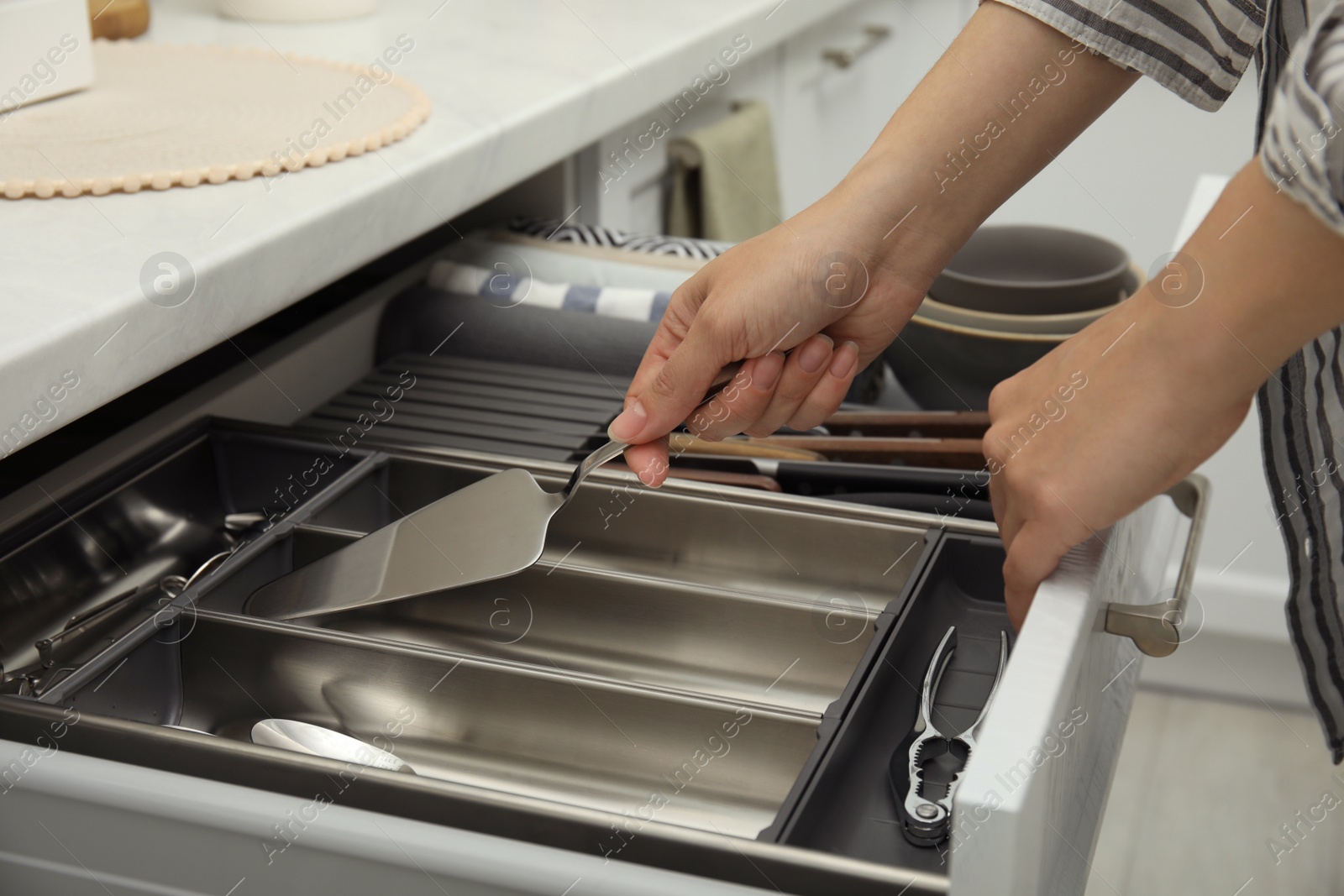 Photo of Woman taking spatula from open drawer of kitchen cabinet, closeup