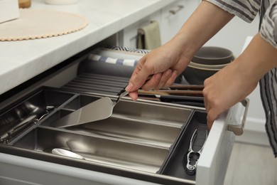 Woman taking spatula from open drawer of kitchen cabinet, closeup