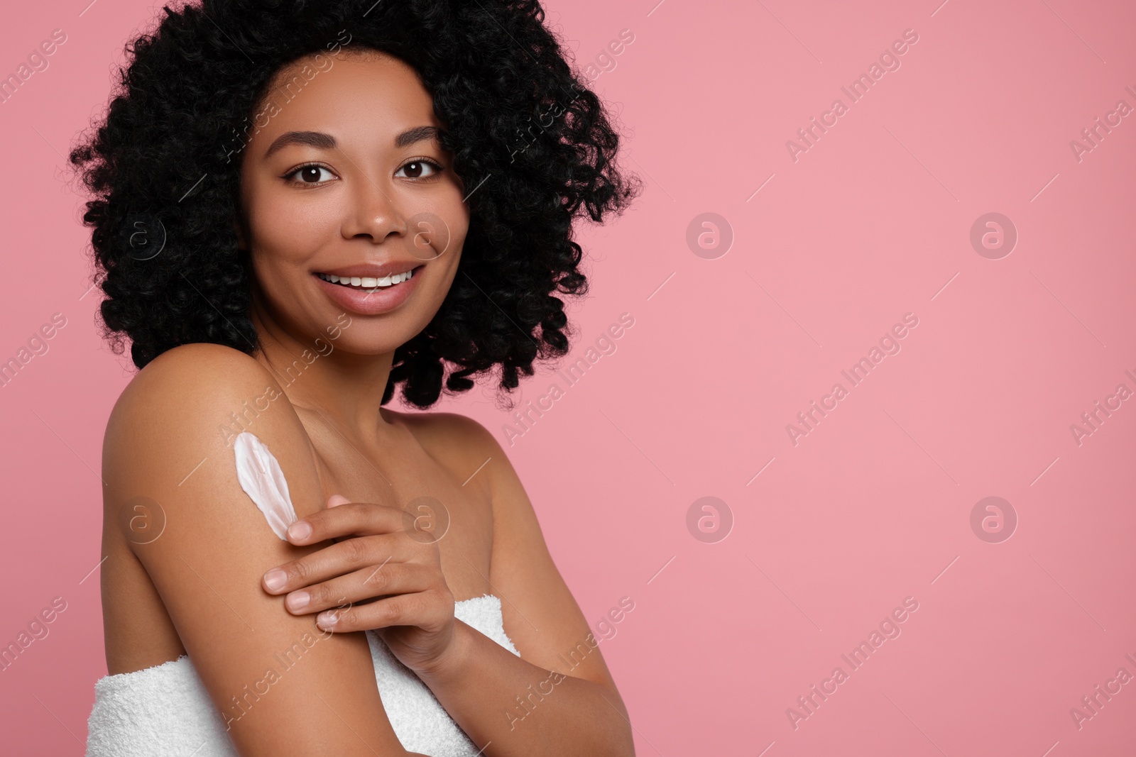 Photo of Young woman applying body cream onto shoulder on pink background. Space for text