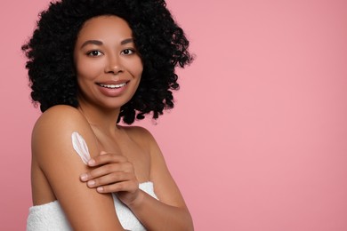 Young woman applying body cream onto shoulder on pink background. Space for text