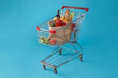Photo of Shopping cart full of groceries on light blue background
