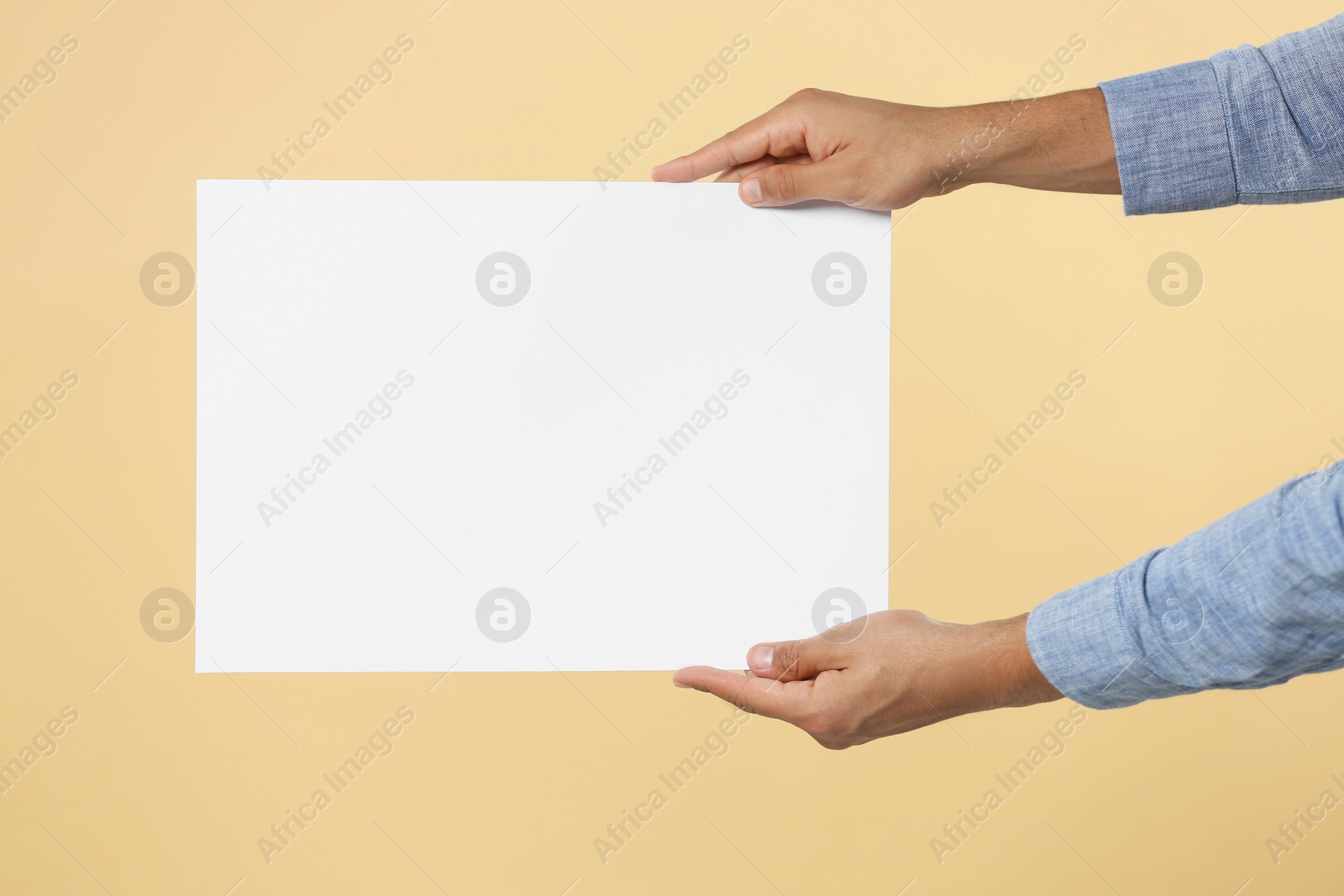 Photo of Man holding sheet of paper on beige background, closeup. Mockup for design