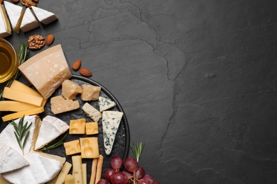 Cheese plate with honey, grapes and nuts on black table, flat lay. Space for text