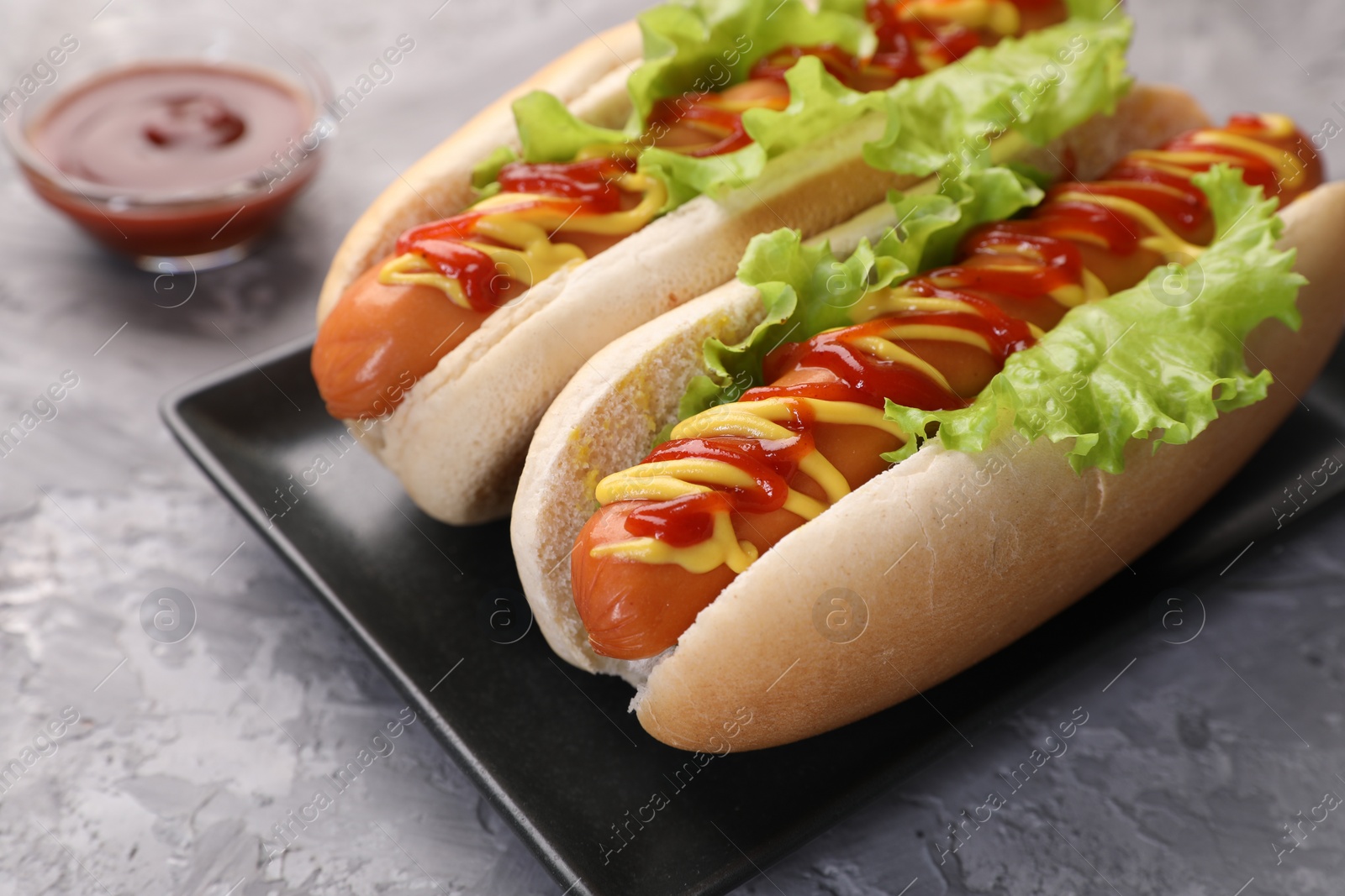 Photo of Tasty hot dogs with lettuce, ketchup and mustard on grey textured table, closeup