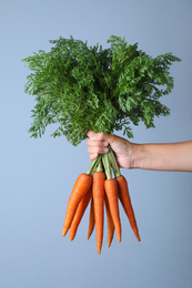 Woman holding ripe carrots on light blue background, closeup