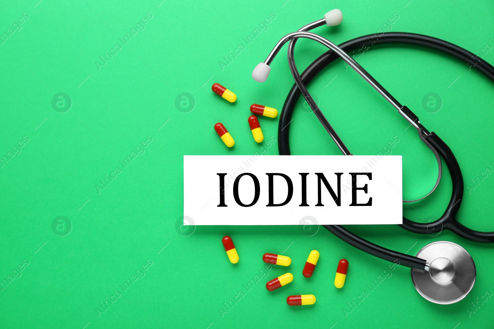 Photo of Card with word Iodine, stethoscope and pills on green background, flat lay. Space for text