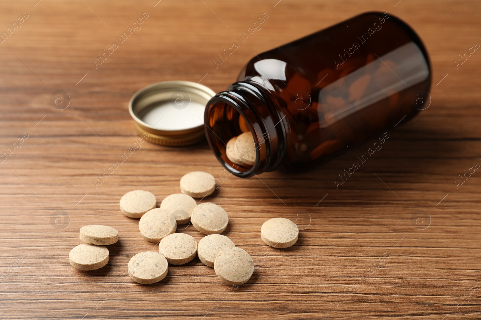 Photo of Overturned bottle with dietary supplement pills on wooden table