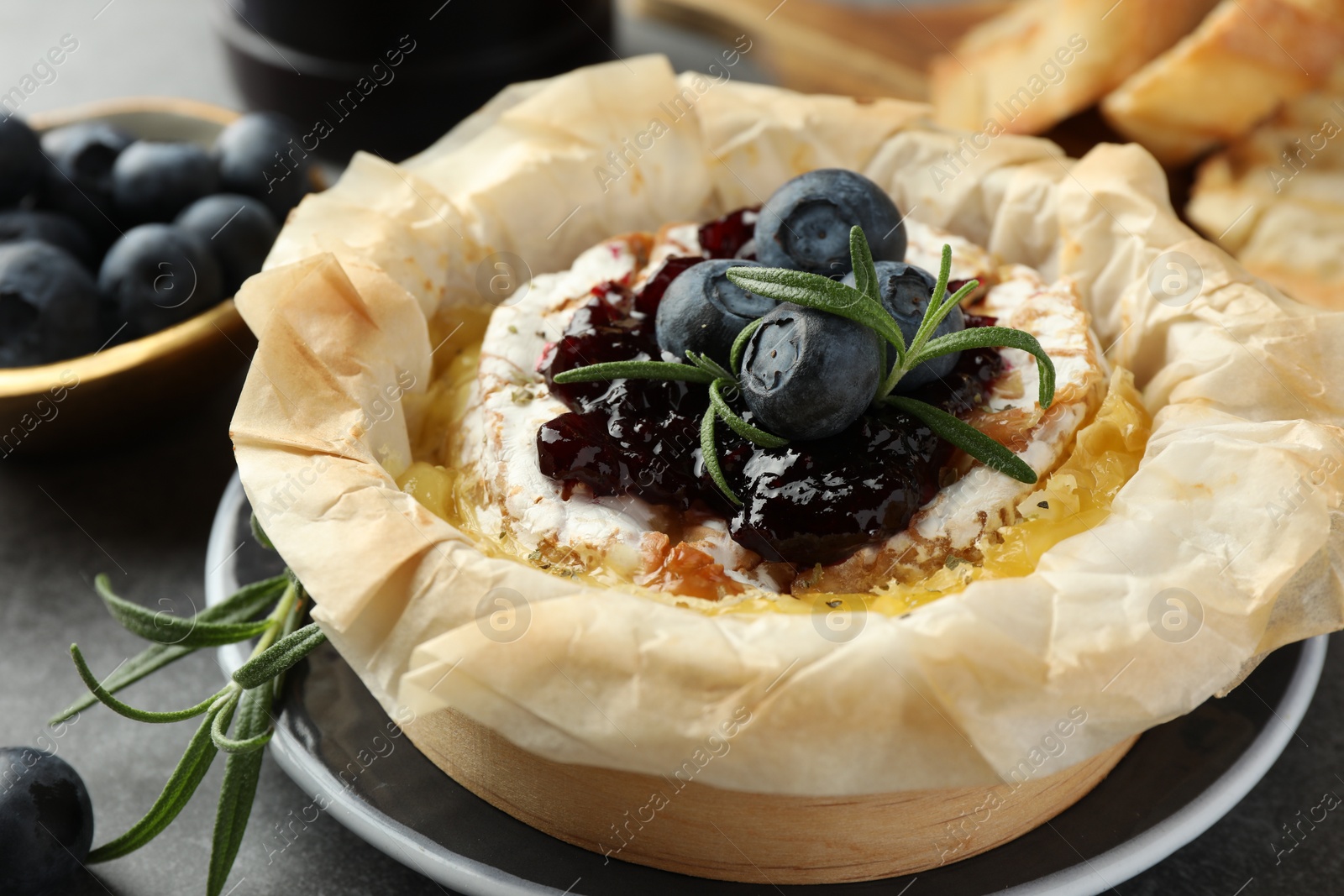 Photo of Tasty baked brie cheese with blueberries, jam and rosemary on grey table, closeup