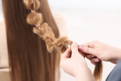 Professional stylist braiding woman's hair on blurred background, closeup