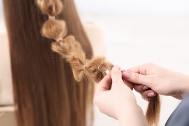 Photo of Professional stylist braiding woman's hair on blurred background, closeup