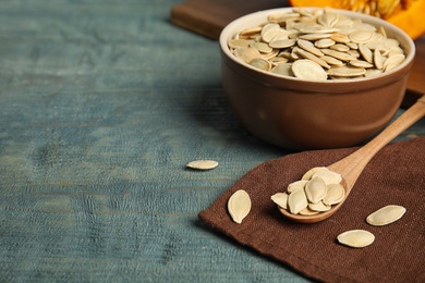 Photo of Raw unpeeled pumpkin seeds on blue wooden table, space for text