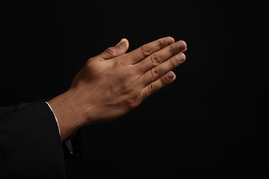 Photo of African American man praying to God on black background, closeup of hands