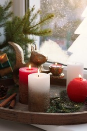 Tray with beautiful burning candles and Christmas decor on windowsill