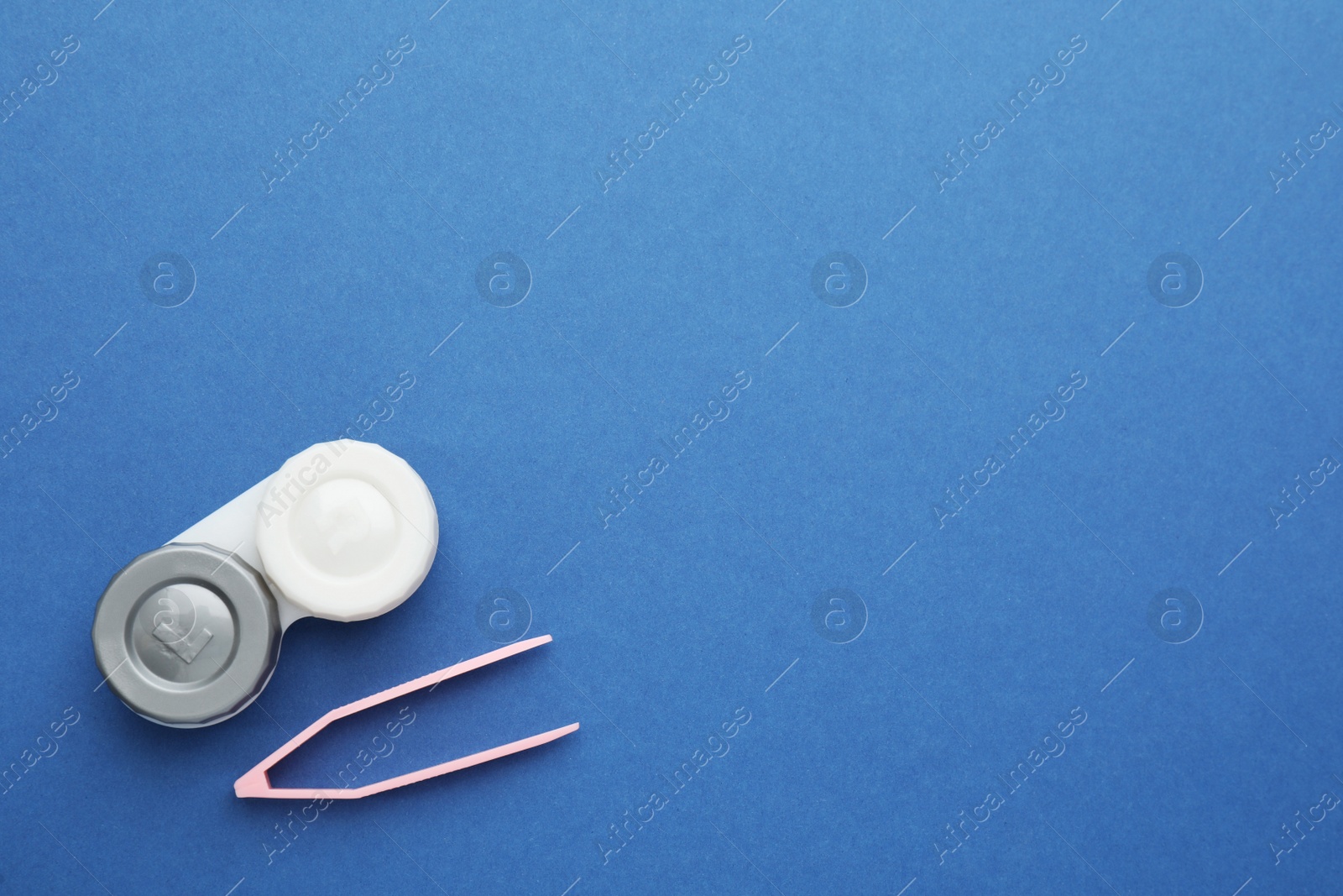 Photo of Case with contact lenses and tweezers on blue background, flat lay. Space for text